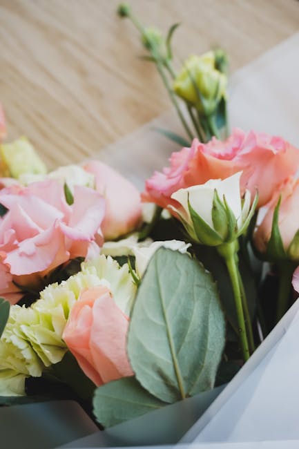 A close-up view of a floral gift featuring a bouquet of fresh light pink and cream lisianthus flowers, complemented by soft green leaves and stems. The flowers are arranged in a natural, loosely gathe